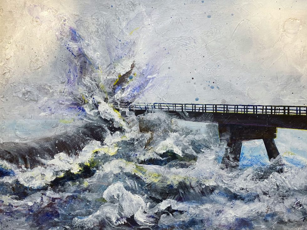 A large wave crashes against a black pier on the beach